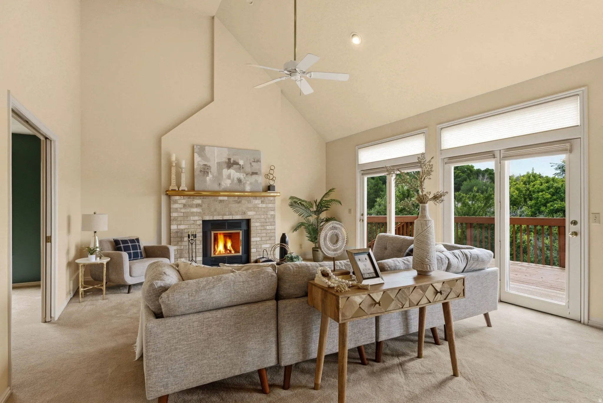 Vaulted ceilings with a ceiling fan, brick fireplace with a wood mantel, glass sliding doors, and light-toned carpet flooring
