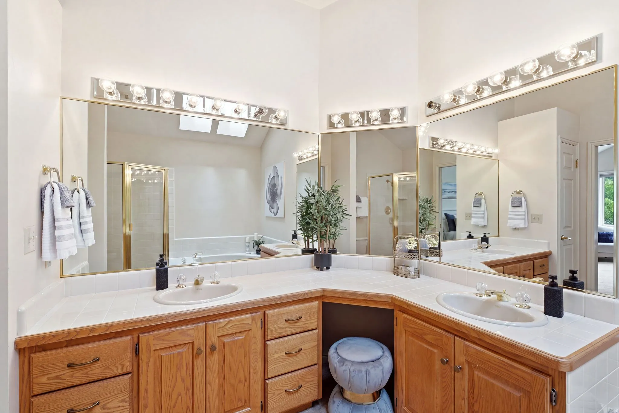 Bathroom vanity featuring dual sinks, wood cabinetry, white tiled countertops, and extensive mirror space