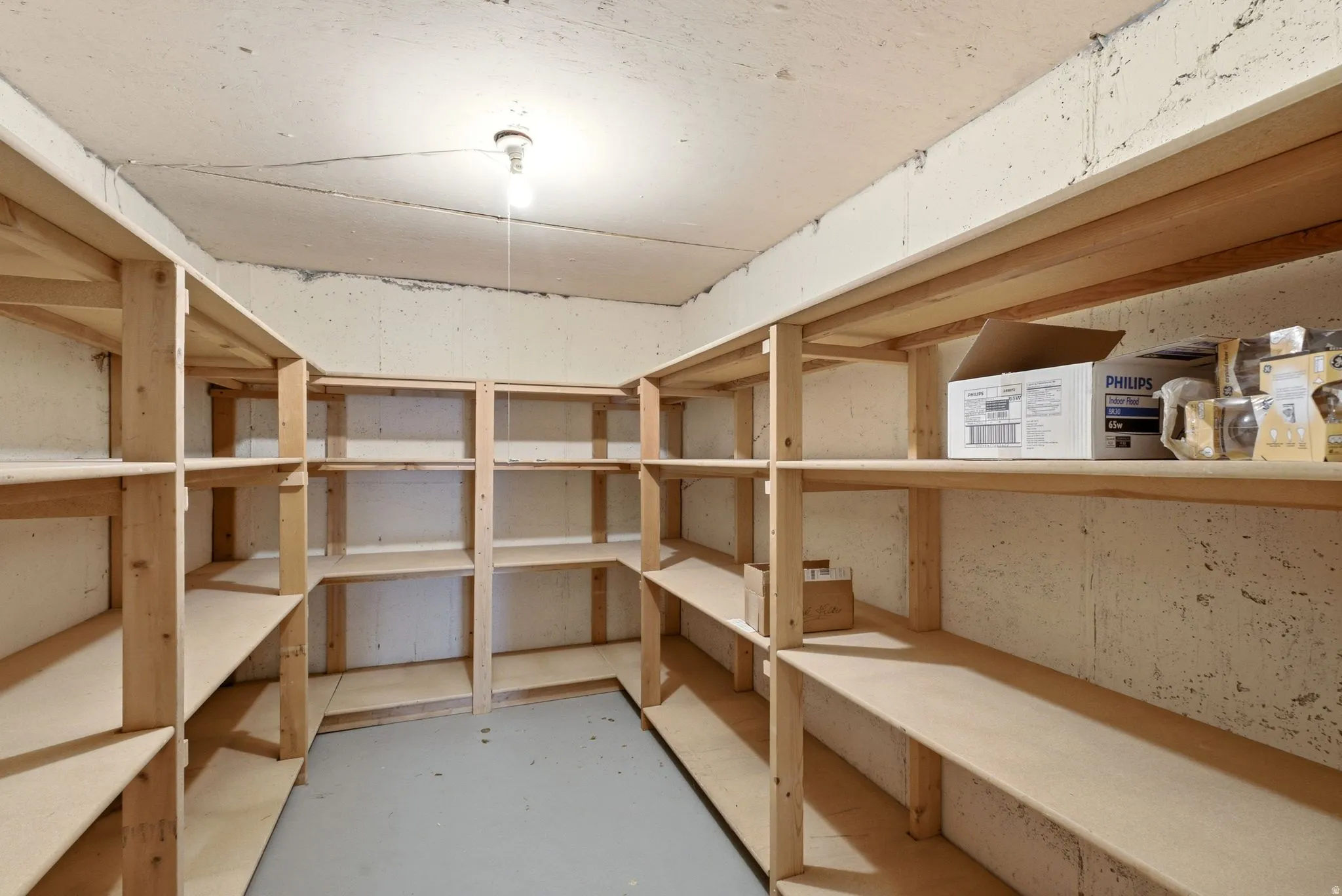 Utility room featuring extensive built-in wooden shelving, concrete walls, and concrete flooring
