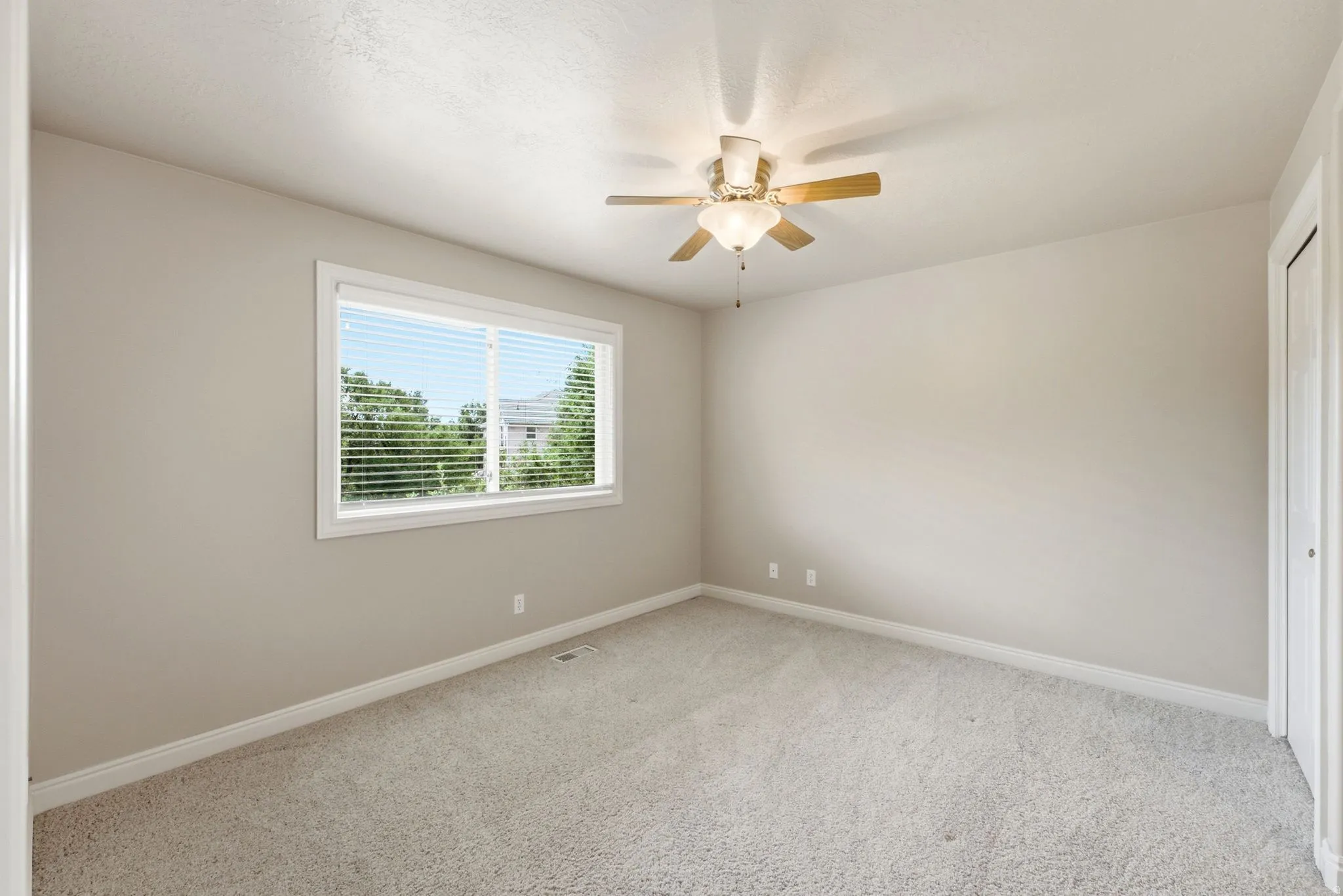 Carpeted room featuring a white-framed window, neutral painted walls, and a ceiling fan with light fixture