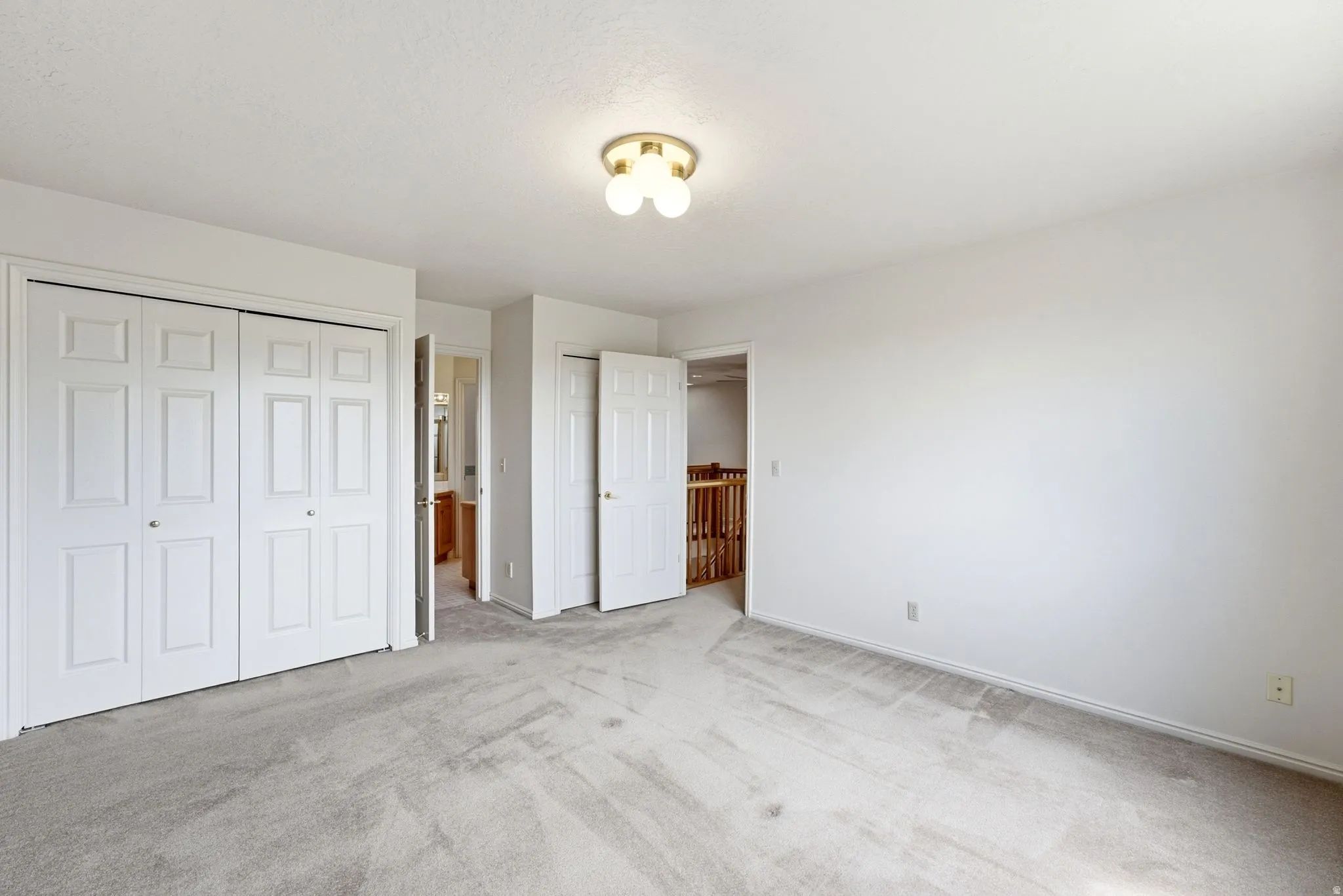Carpeted room featuring a ceiling-mounted light fixture, two bi-fold closet doors, and painted white walls