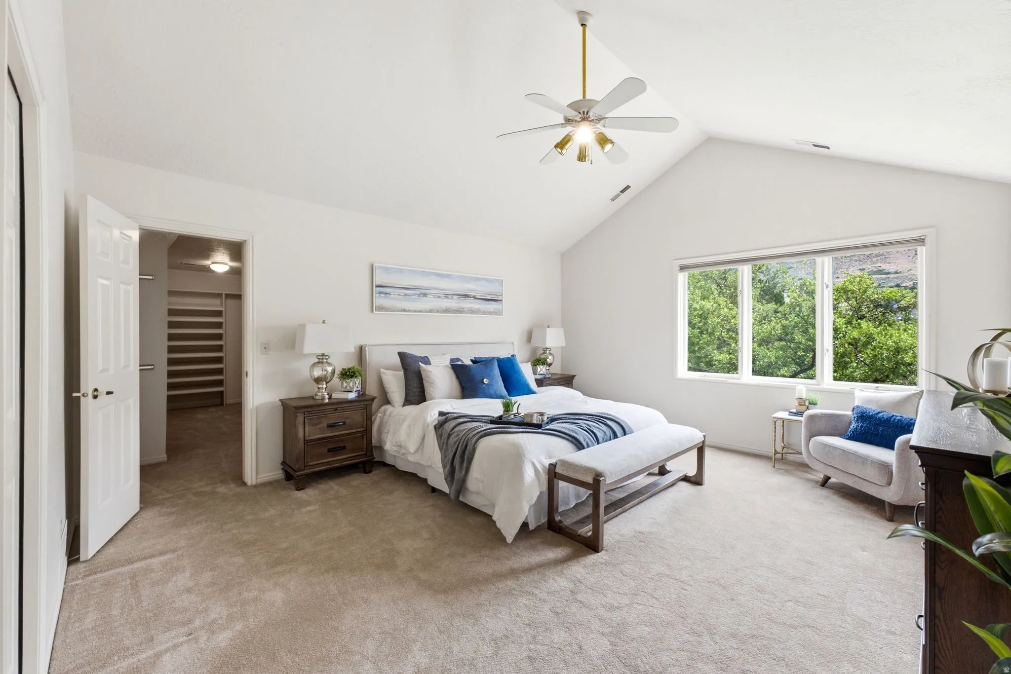 Spacious room featuring vaulted ceilings, a large window overlooking lush trees, and light tan carpeting