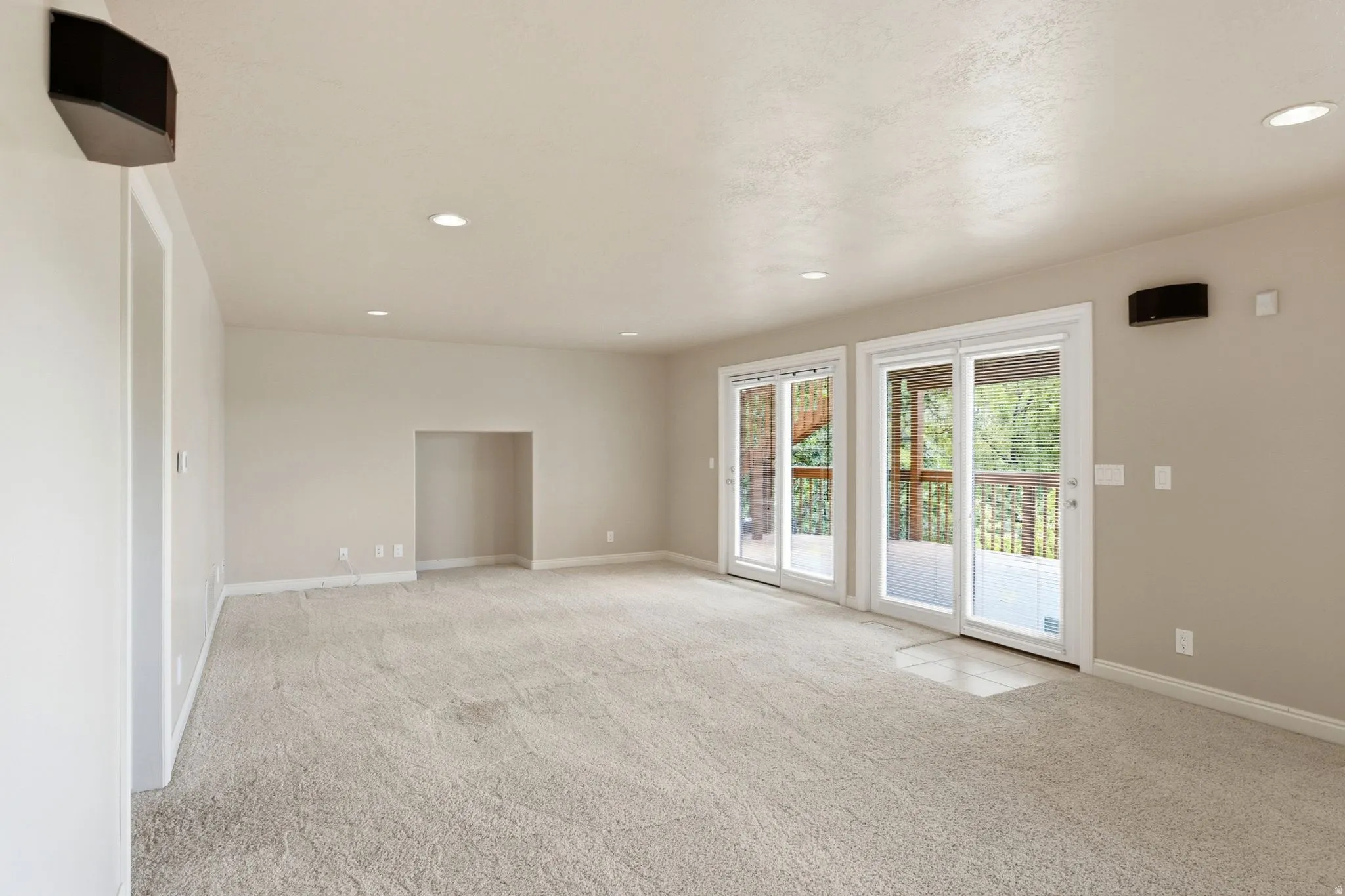 Spacious interior featuring two sets of glass sliding doors, recessed lighting, wall-mounted speakers, a neutral carpeted floor, and a built-in wall niche