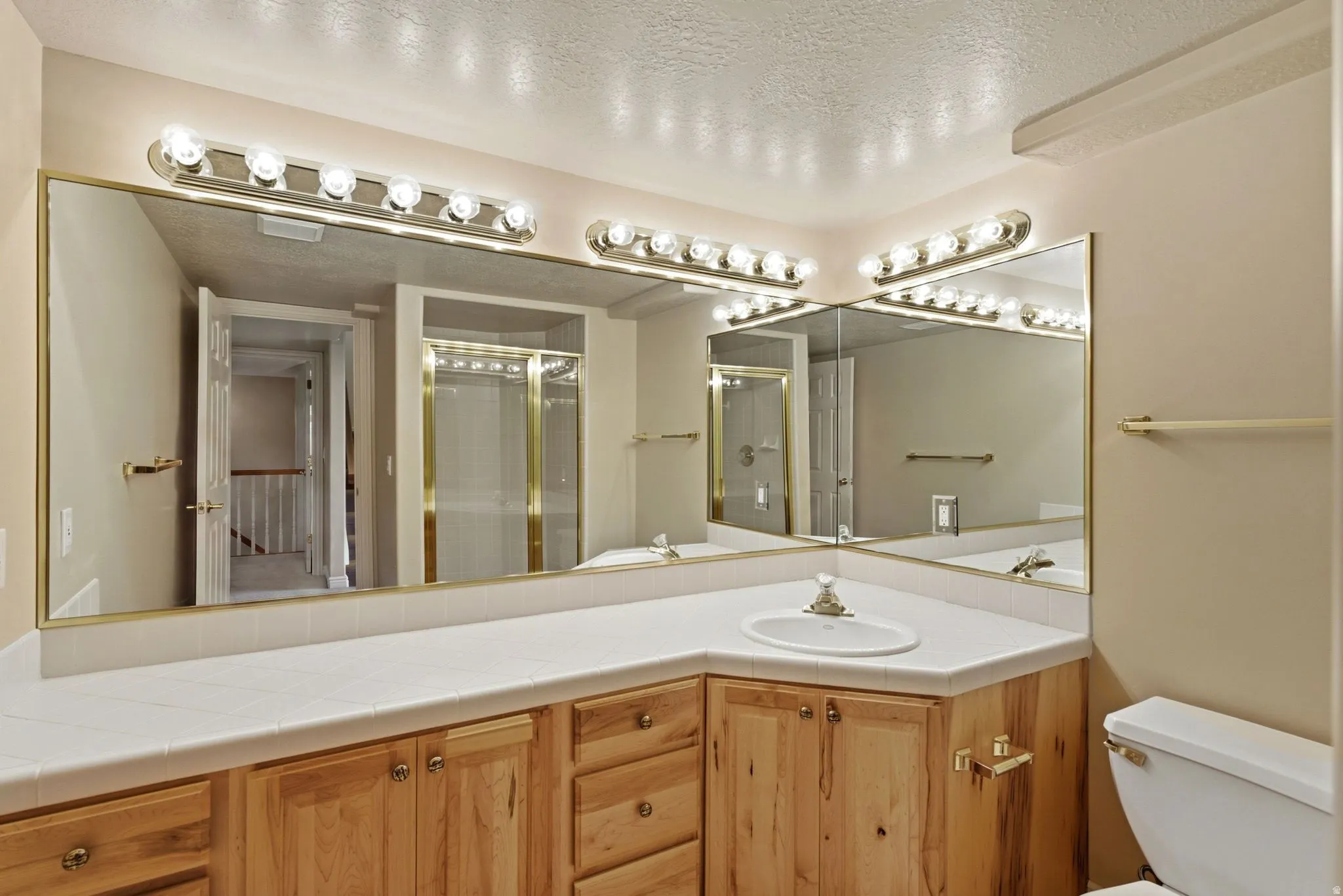 Dual vanity mirrors with brass-finish framing, integrated vanity lighting, wood-finish cabinetry, a single basin sink, and a toilet