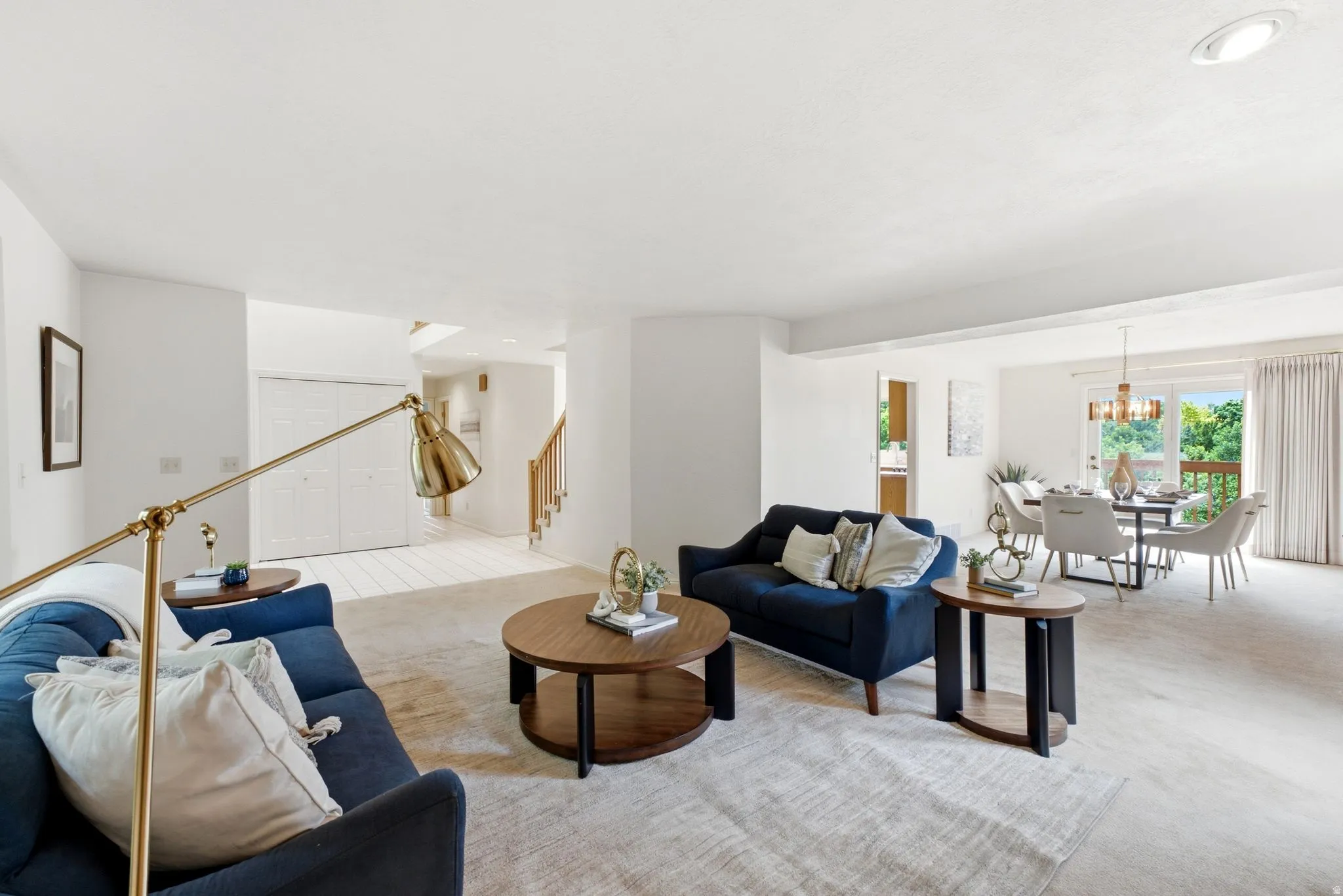 Open-concept living space featuring light-toned carpeting, a dining area with a contemporary chandelier, and a sliding glass door leading to an outdoor area