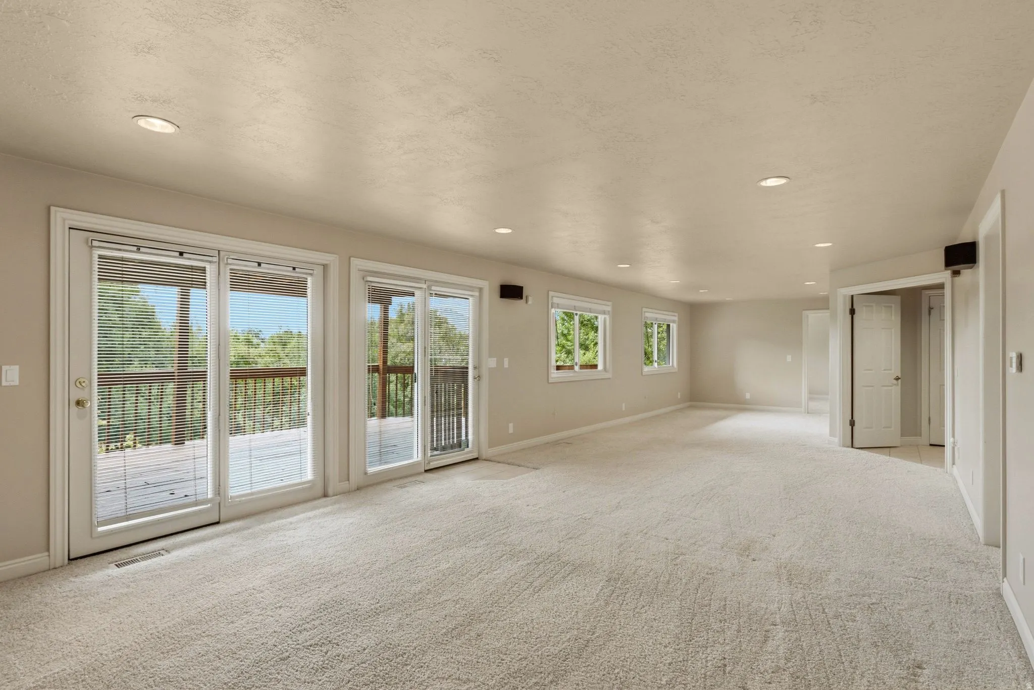 Recessed lighting, light-toned carpeting, multiple glass doors, and a neutral color palette