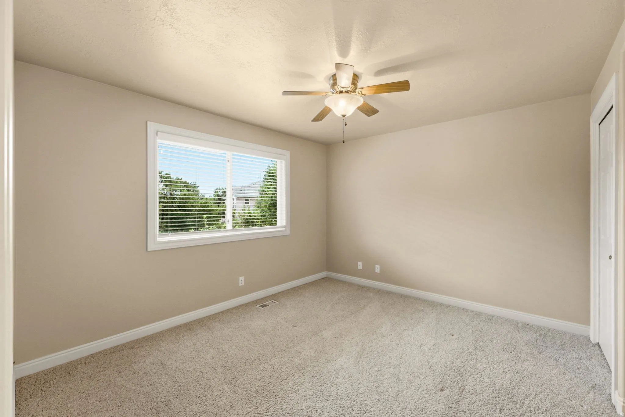 Neutral-toned walls, light-colored carpeting, a ceiling fan with integrated lighting, and a white-framed window