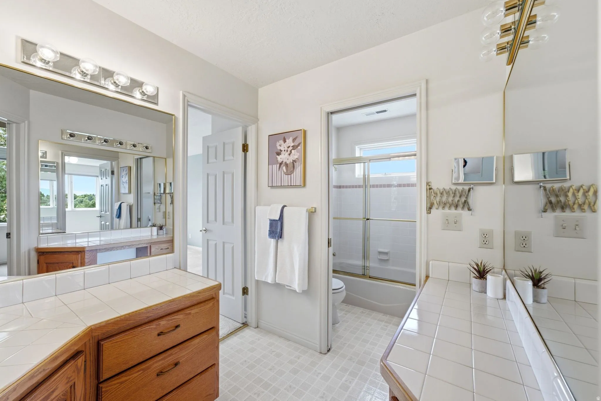 Bathroom featuring a tiled countertop, wood-finish cabinetry, full-width mirror, and a shower-tub combination with a sliding glass door