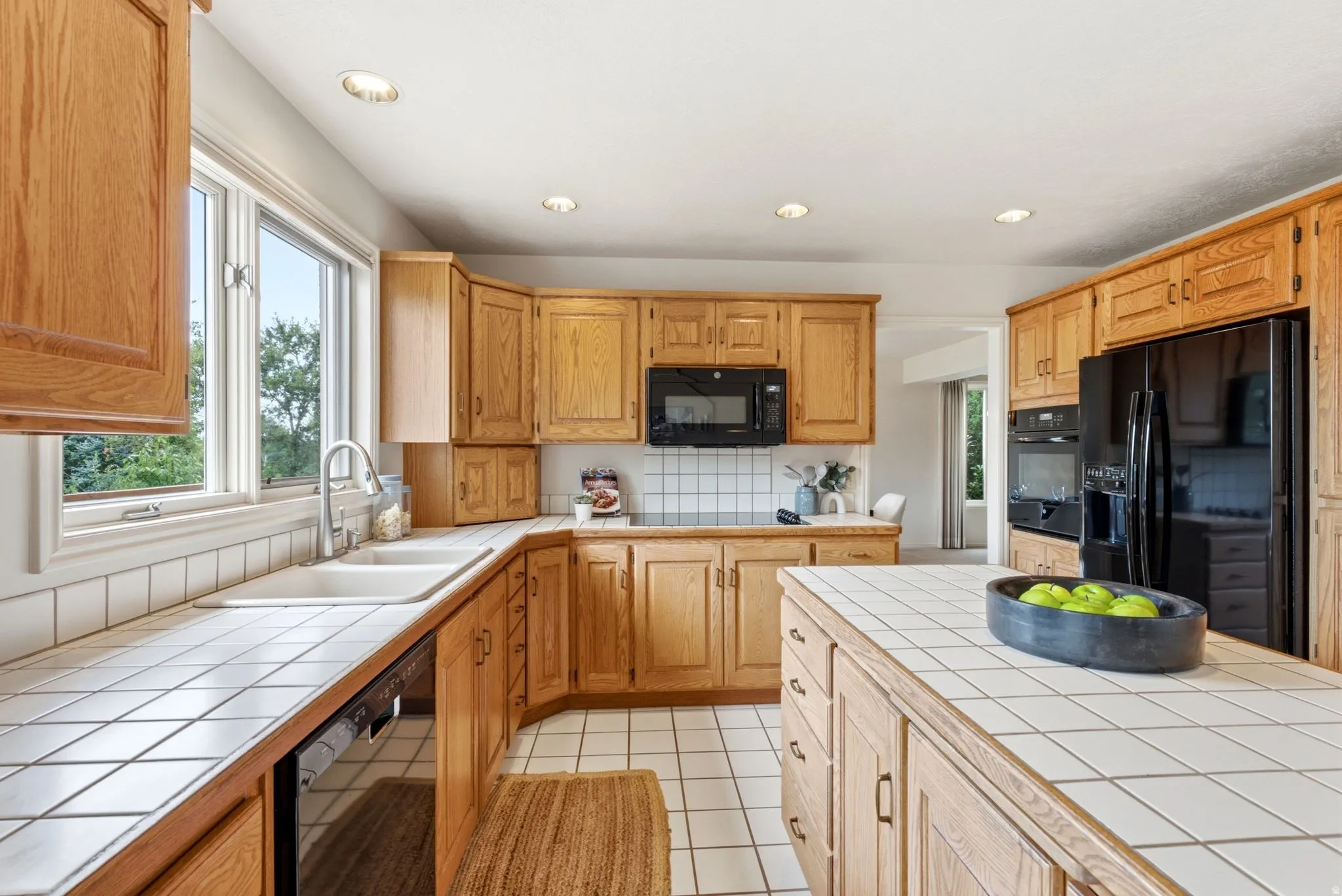 Kitchen featuring abundant wood cabinetry, a central island with tile countertop, integrated black appliances, and recessed lighting