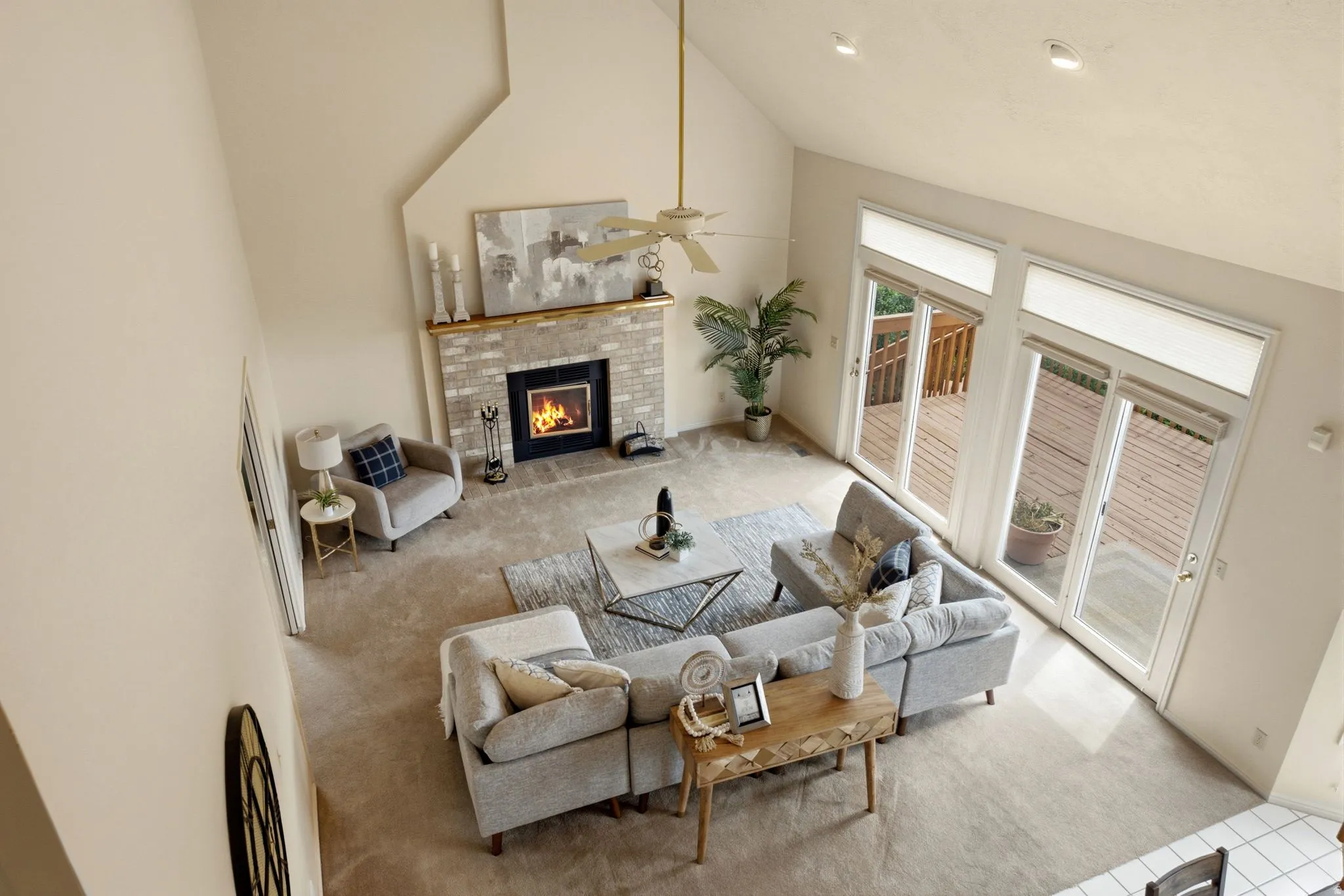 Vaulted ceiling, brick fireplace with wood mantel, ceiling fan, carpeted flooring, and sliding glass doors with transom windows
