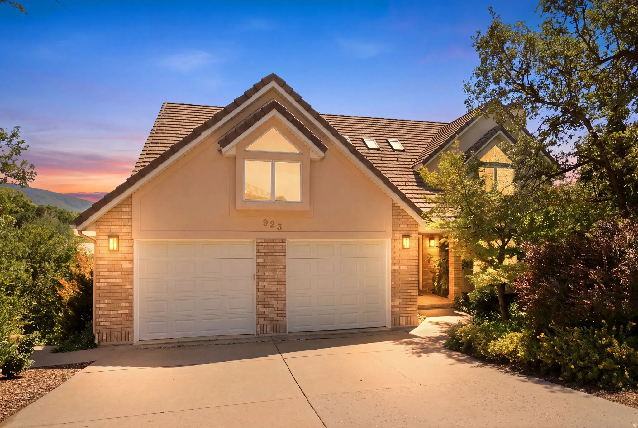 Stucco and brick facade residence featuring a two-car garage, pitched tile roof, and dormer window
