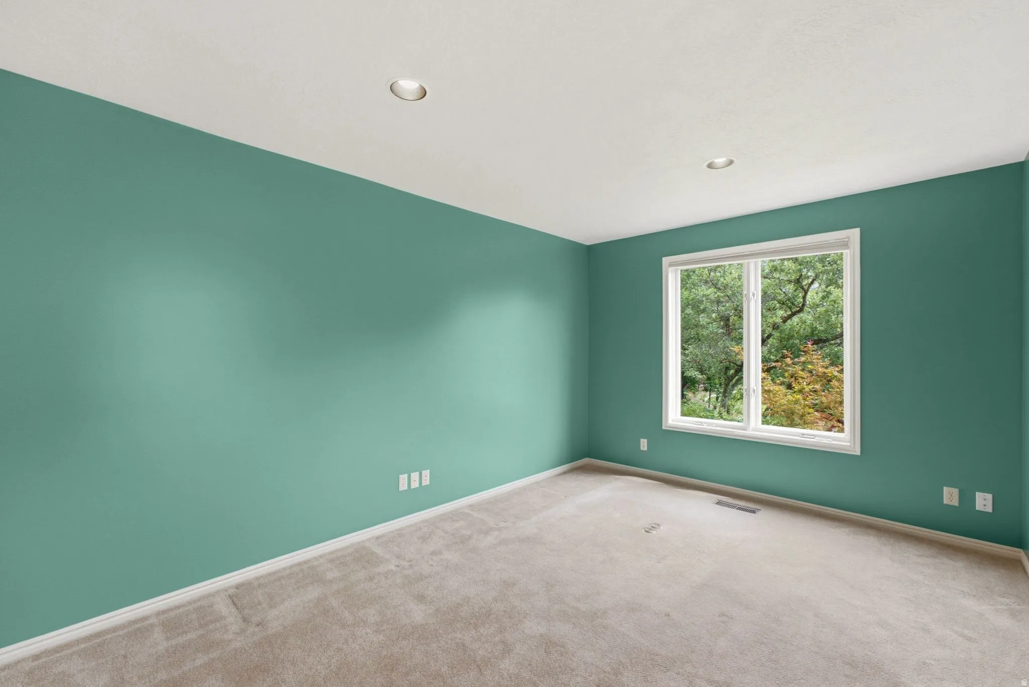 Recessed lighting, large window with white trim, light-colored carpeting, green painted walls, and white electrical outlets