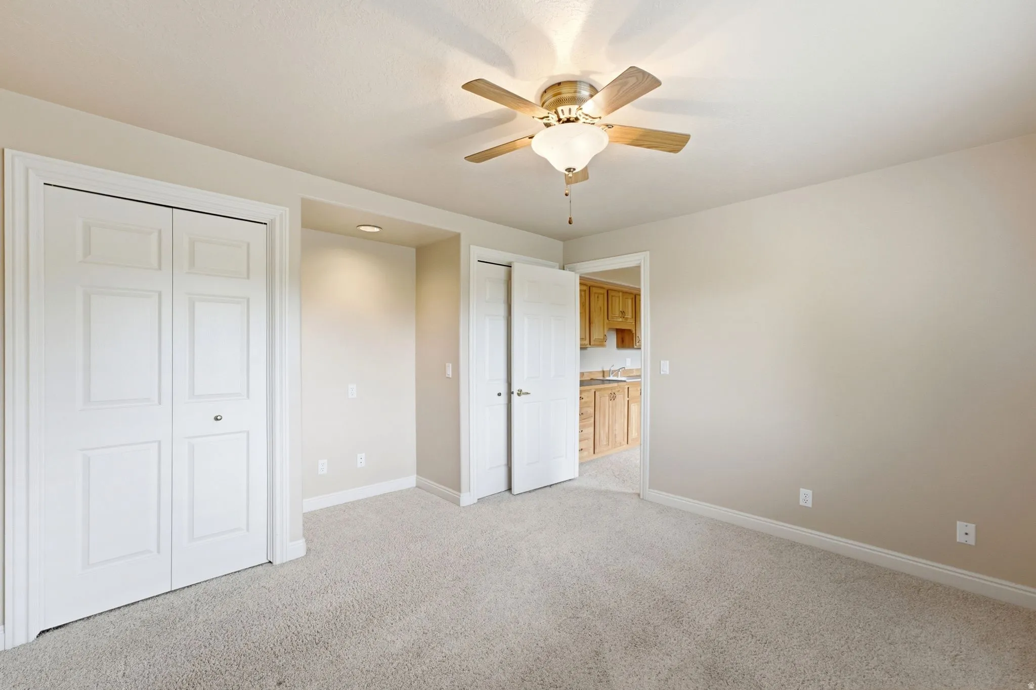 Neutral-toned room featuring light-colored carpet flooring, a ceiling fan with integrated lighting, and multiple panel bi-fold closet doors