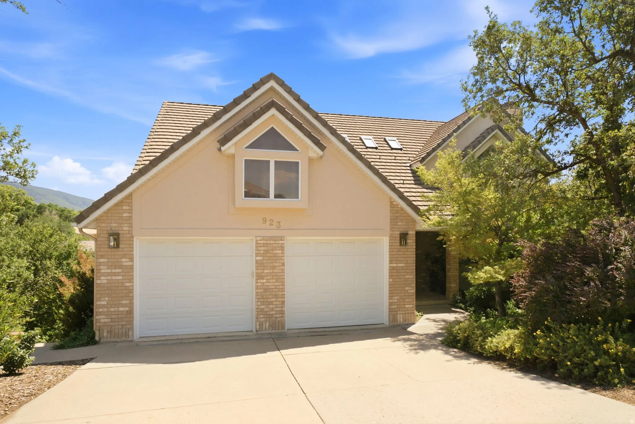Stucco and brick facade residence featuring a two-car garage, pitched tile roof, and a prominent dormer window