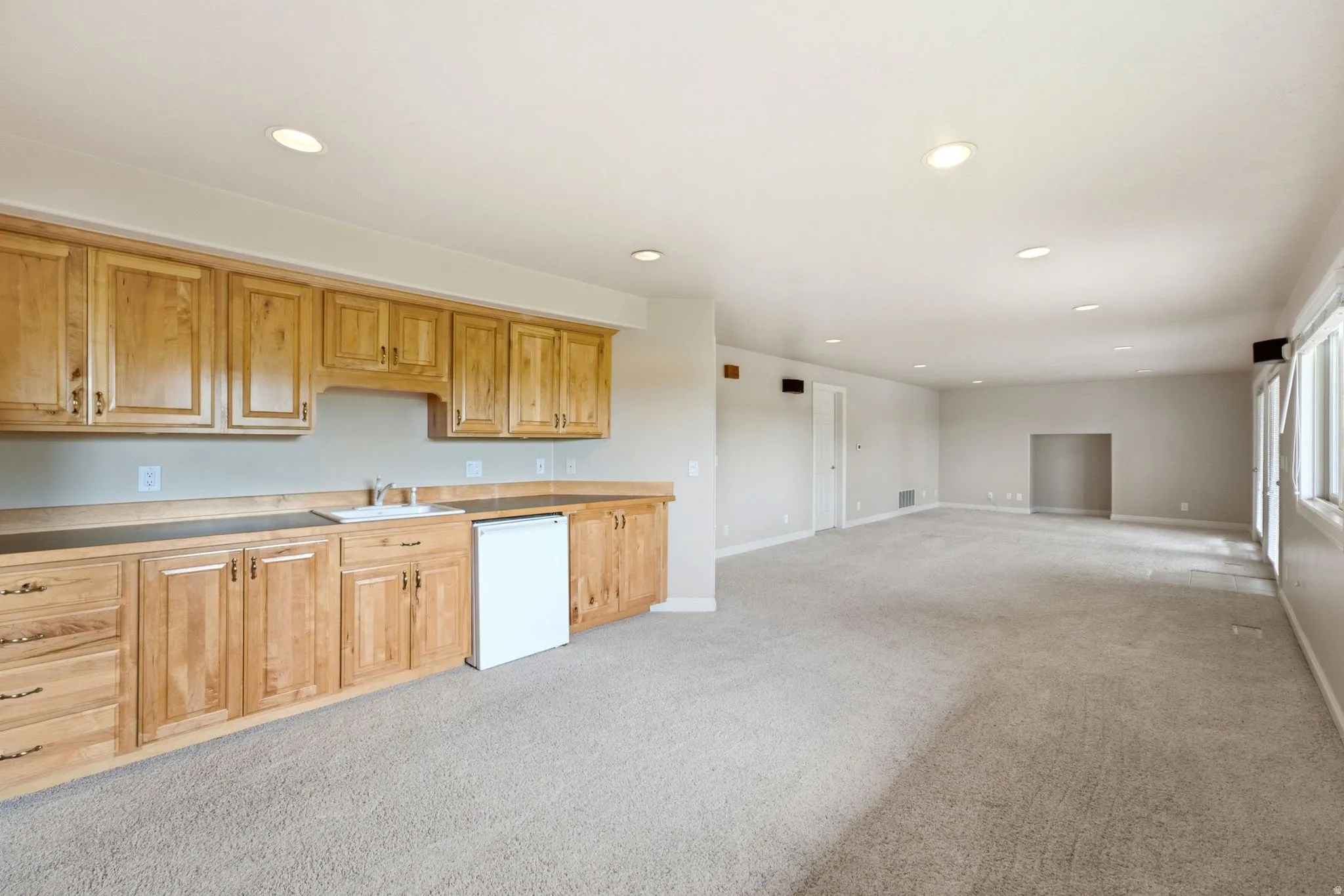 Spacious room featuring light wood cabinetry with a sink, under-counter refrigerator, and ample countertop space