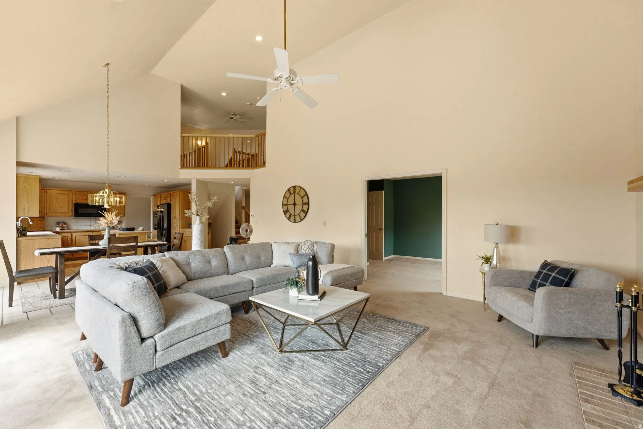 Vaulted ceilings with a ceiling fan, a kitchen with wood cabinetry, and a carpeted living area