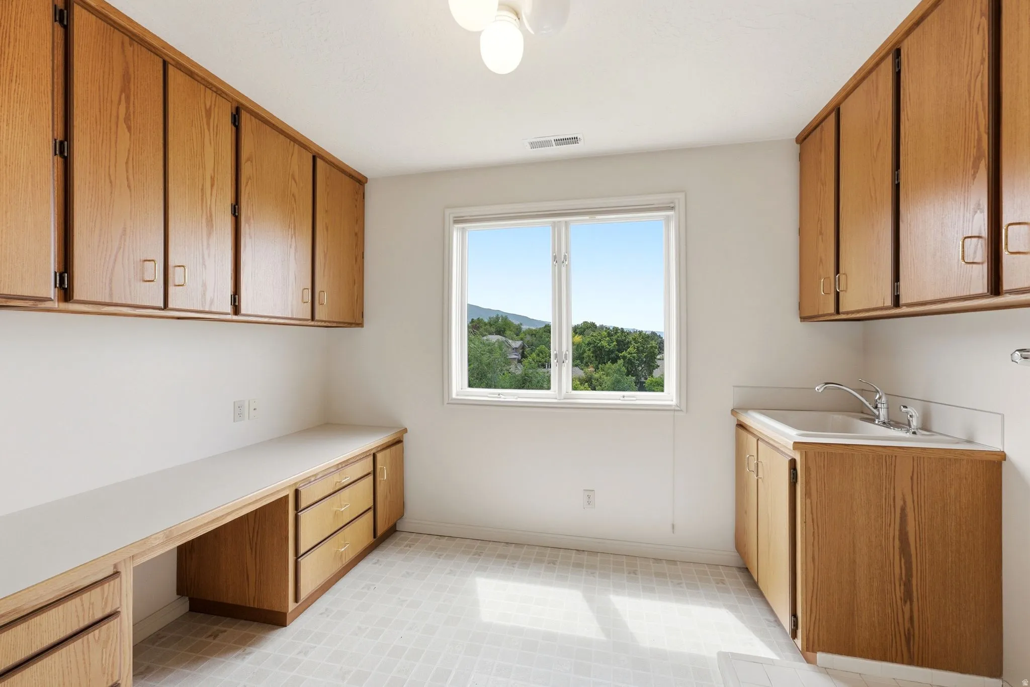 Utility room featuring a double-pane window, extensive oak-finish cabinetry, a built-in countertop, and a utility sink with a chrome faucet