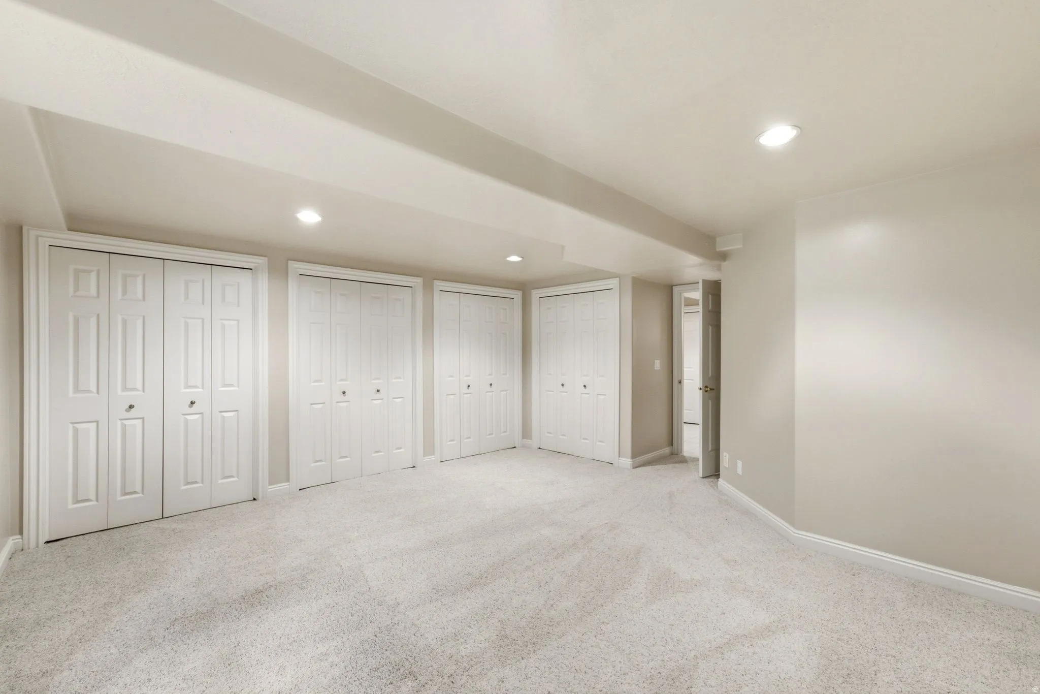 Spacious room featuring light-colored carpeting, multiple bifold closet doors, recessed lighting, and neutral wall tones