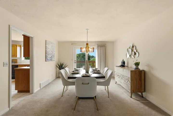 Carpeted dining area with a brass-toned chandelier and light-colored walls