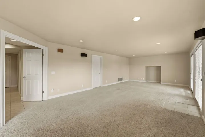Spacious room featuring neutral carpeting, recessed lighting, double French doors with blinds, and an integrated wall niche