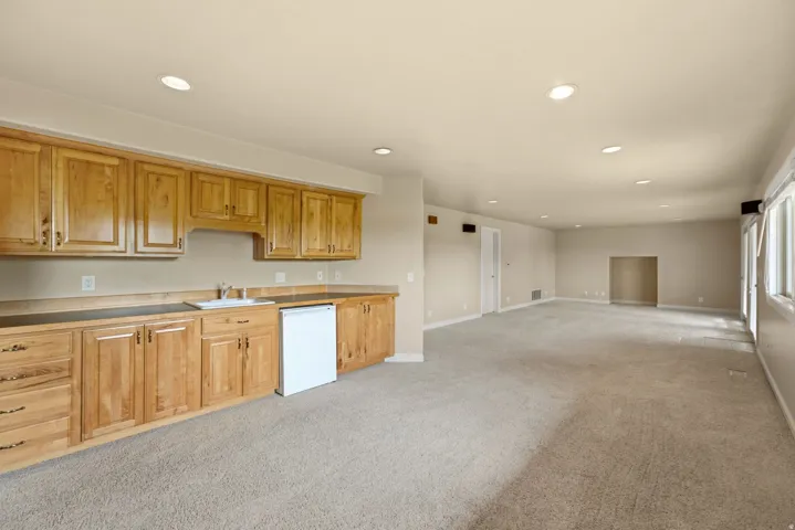 Integrated wet bar featuring a sink, wood cabinetry, and a compact refrigerator