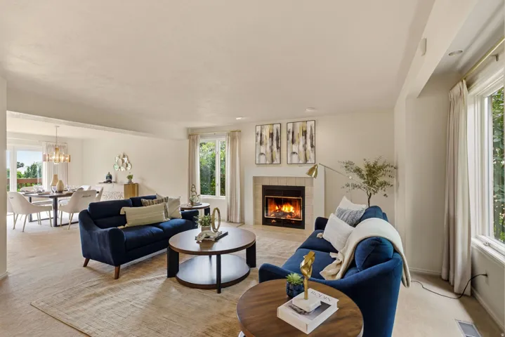 Living area featuring a fireplace with a light-colored tile surround, large windows, and an open layout connecting to a dining space