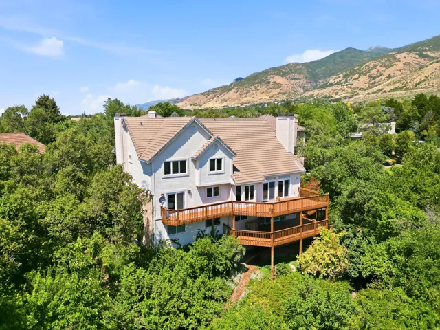 Multi-level residence featuring a terraced wood-finish deck, multiple glass-paned doors, and a tiled roof
