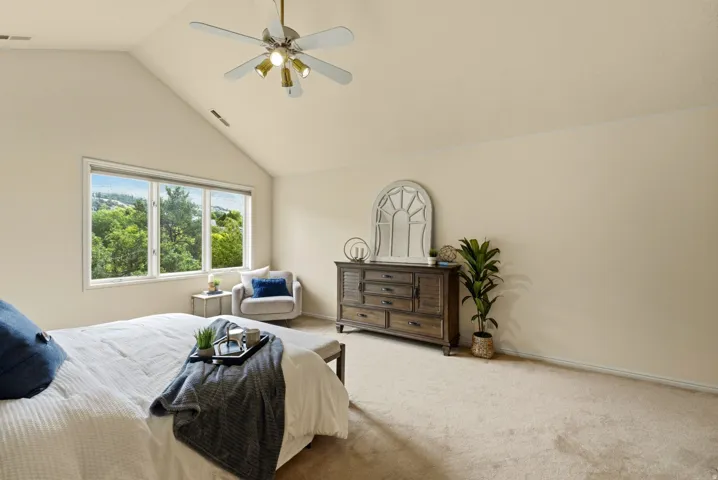 Vaulted ceiling with ceiling fan, large multi-pane window, and carpeted flooring
