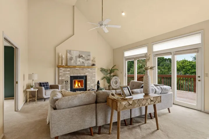 Vaulted ceilings with a ceiling fan, brick fireplace with a wood mantel, glass sliding doors, and light-toned carpet flooring