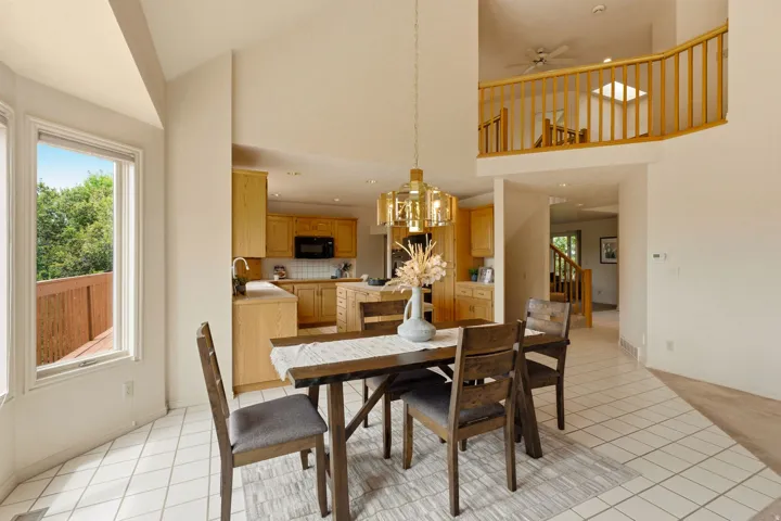 Vaulted ceiling, open kitchen, kitchen island with built-in cabinetry, light wood-finish cabinetry, and a balcony with wood railing