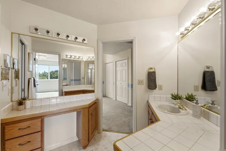 Dual vanity with integrated sinks, tile countertops, wood-finish cabinetry, and overhead lighting fixtures