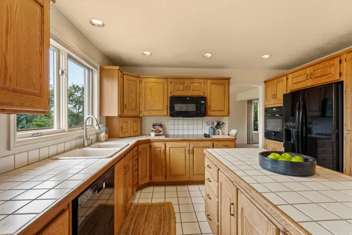 Kitchen featuring wood cabinetry, white tile countertops, recessed lighting, and black appliances