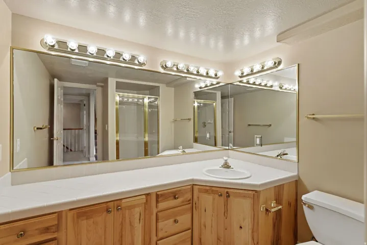 Dual vanity mirrors with brass-finish framing, integrated vanity lighting, wood-finish cabinetry, a single basin sink, and a toilet