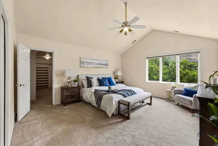 Vaulted ceiling, ceiling fan with integrated lighting, large window, carpeted flooring, built-in closet shelving