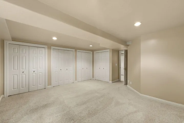 Recessed lighting illuminates the carpeted flooring and multiple bi-fold closet doors