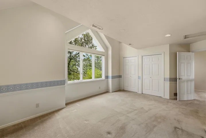 Vaulted ceiling, two paneled closet doors, carpeted flooring, large window, additional door