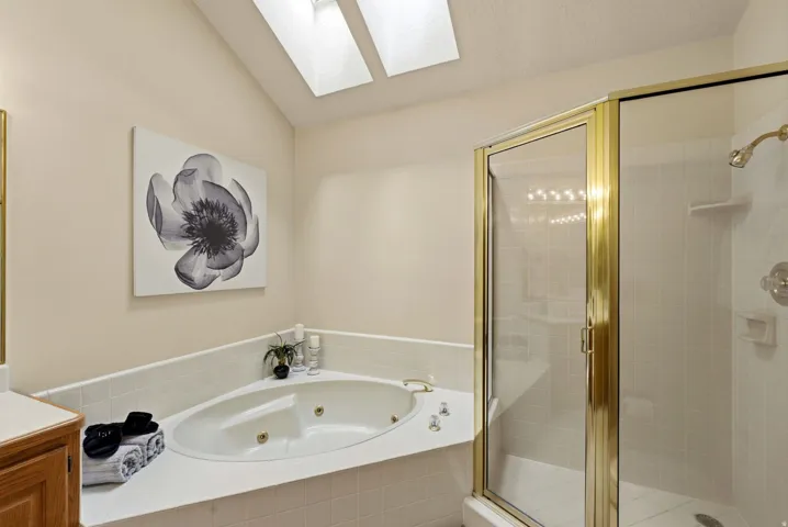 Built-in soaking tub with corner placement, glass-enclosed shower with gold-tone framing, and dual skylights