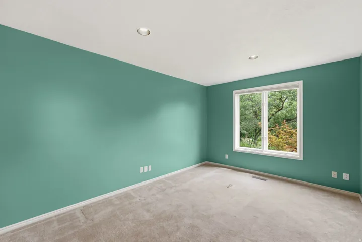 Recessed lighting, large window with white trim, light-colored carpeting, green painted walls, and white electrical outlets
