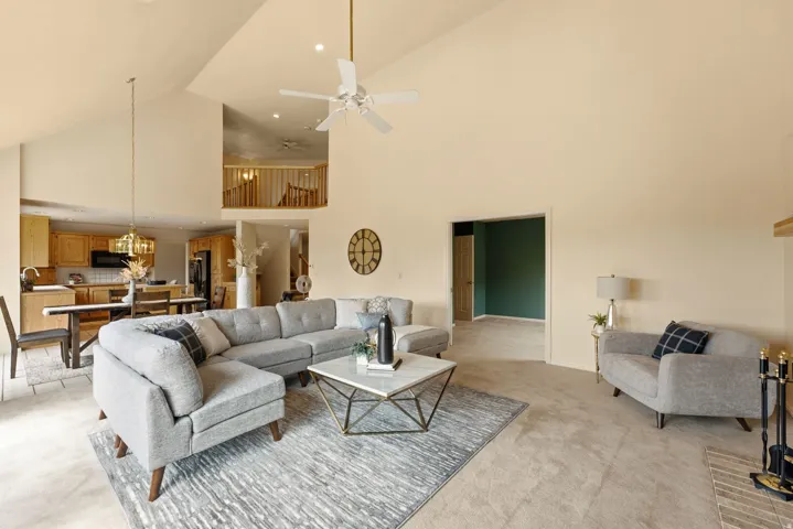 Vaulted ceilings with a ceiling fan, a kitchen with wood cabinetry, and a carpeted living area