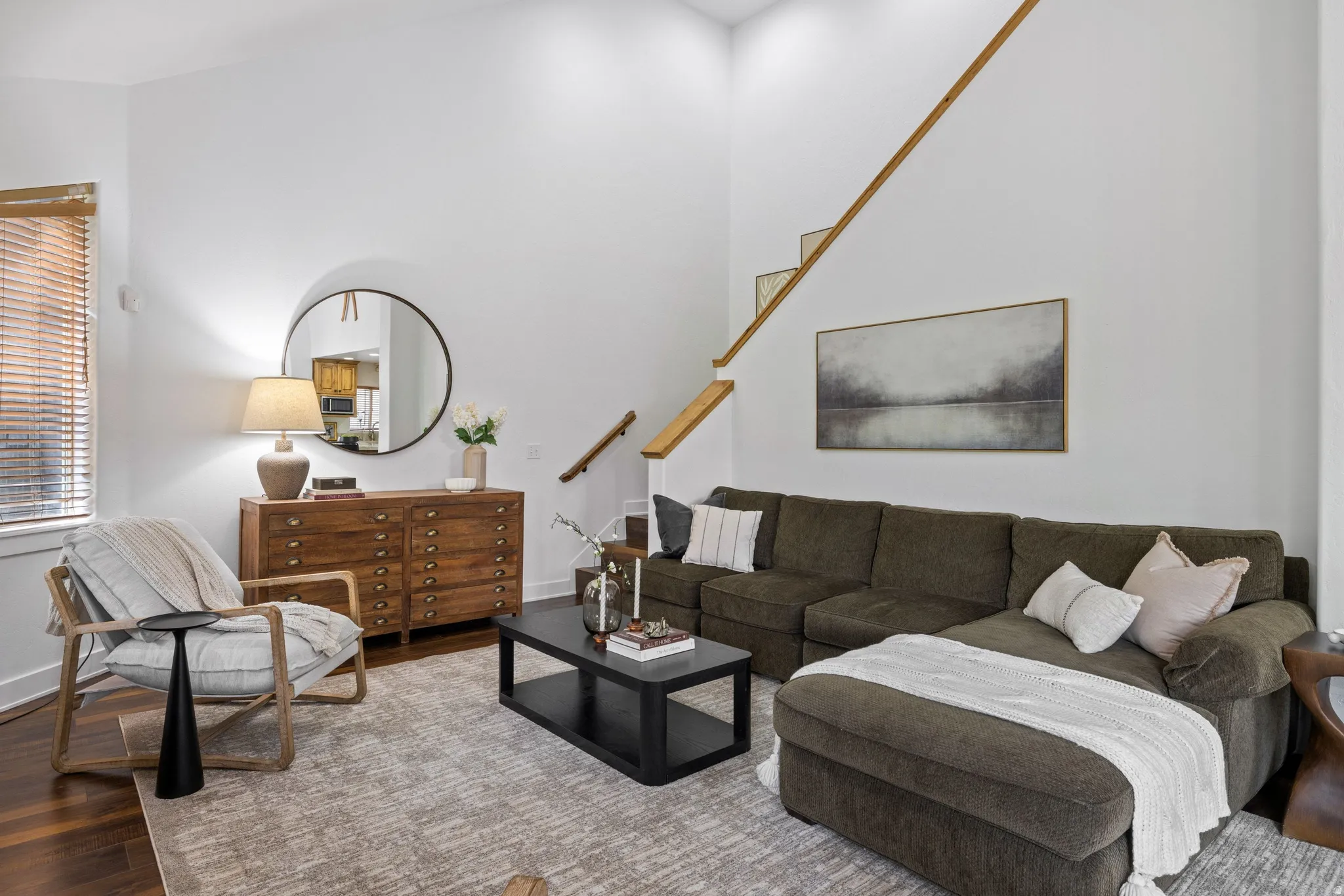 Vaulted ceiling living area featuring hardwood flooring, a staircase with wood handrails, and a window with wood blinds