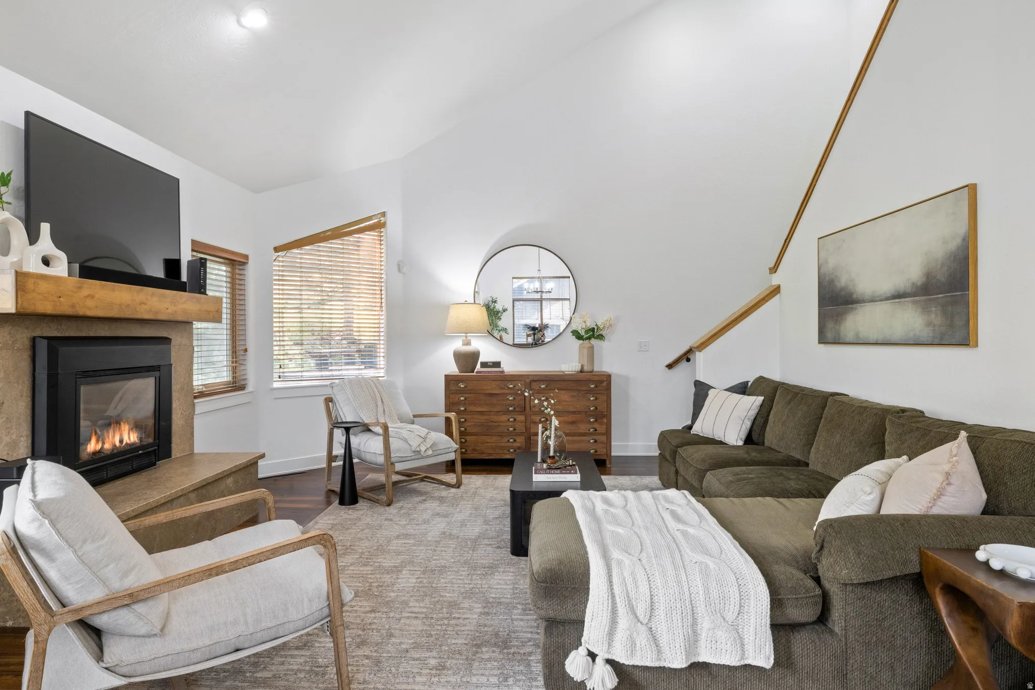 Living area featuring a stone-clad fireplace with a wood mantel, vaulted ceilings, and wood-finish flooring
