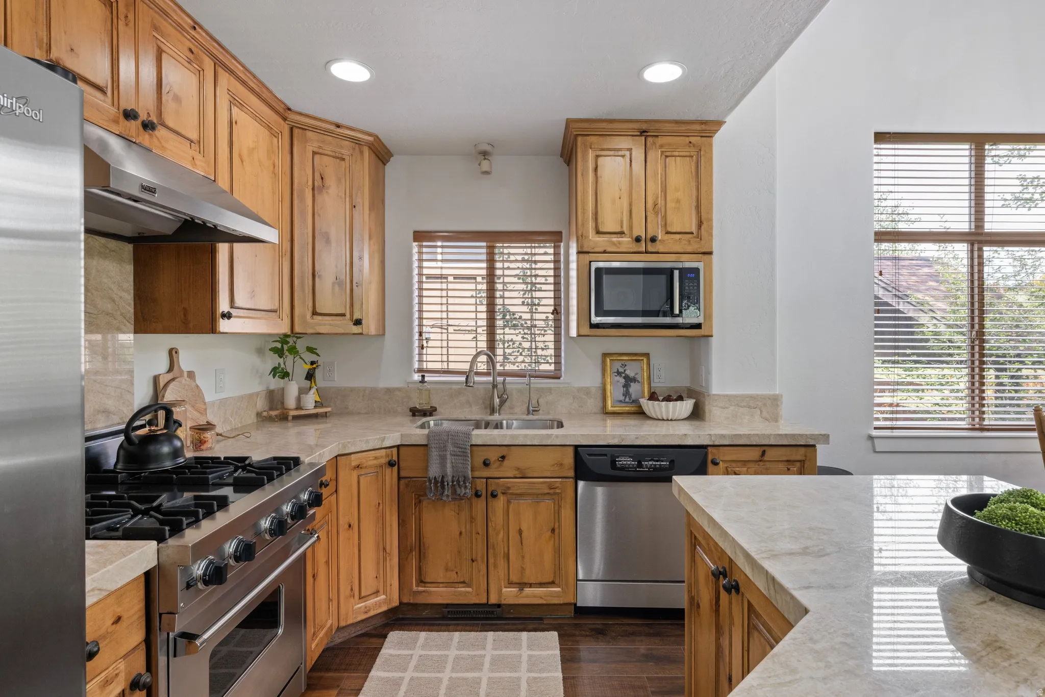 Kitchen featuring natural wood cabinetry, light-toned countertops, stainless steel appliances, and wood-finish flooring