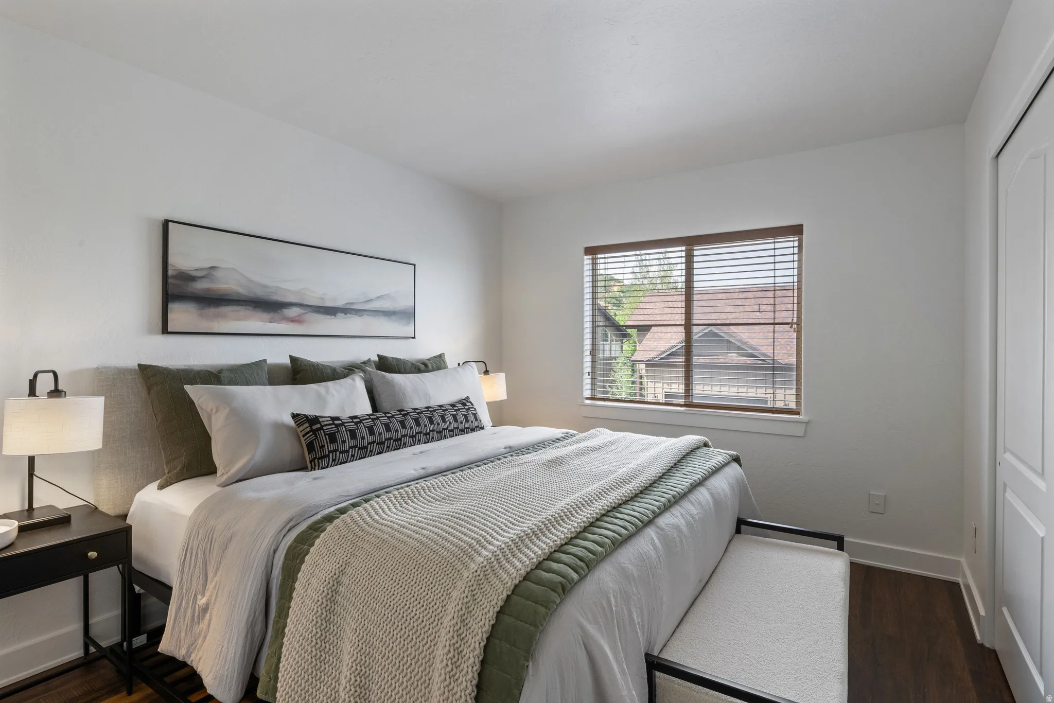 Bedroom featuring wood-finish flooring, white walls, and a window with wood blinds