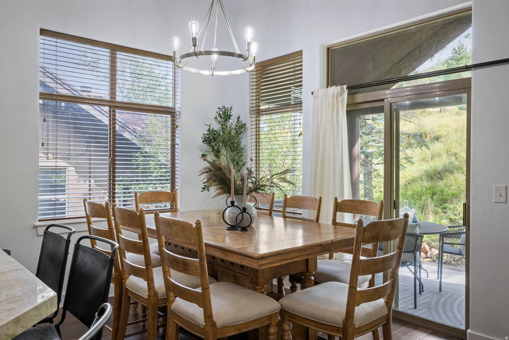 Dining area featuring wood-finish flooring, a contemporary chandelier, and large windows with blinds