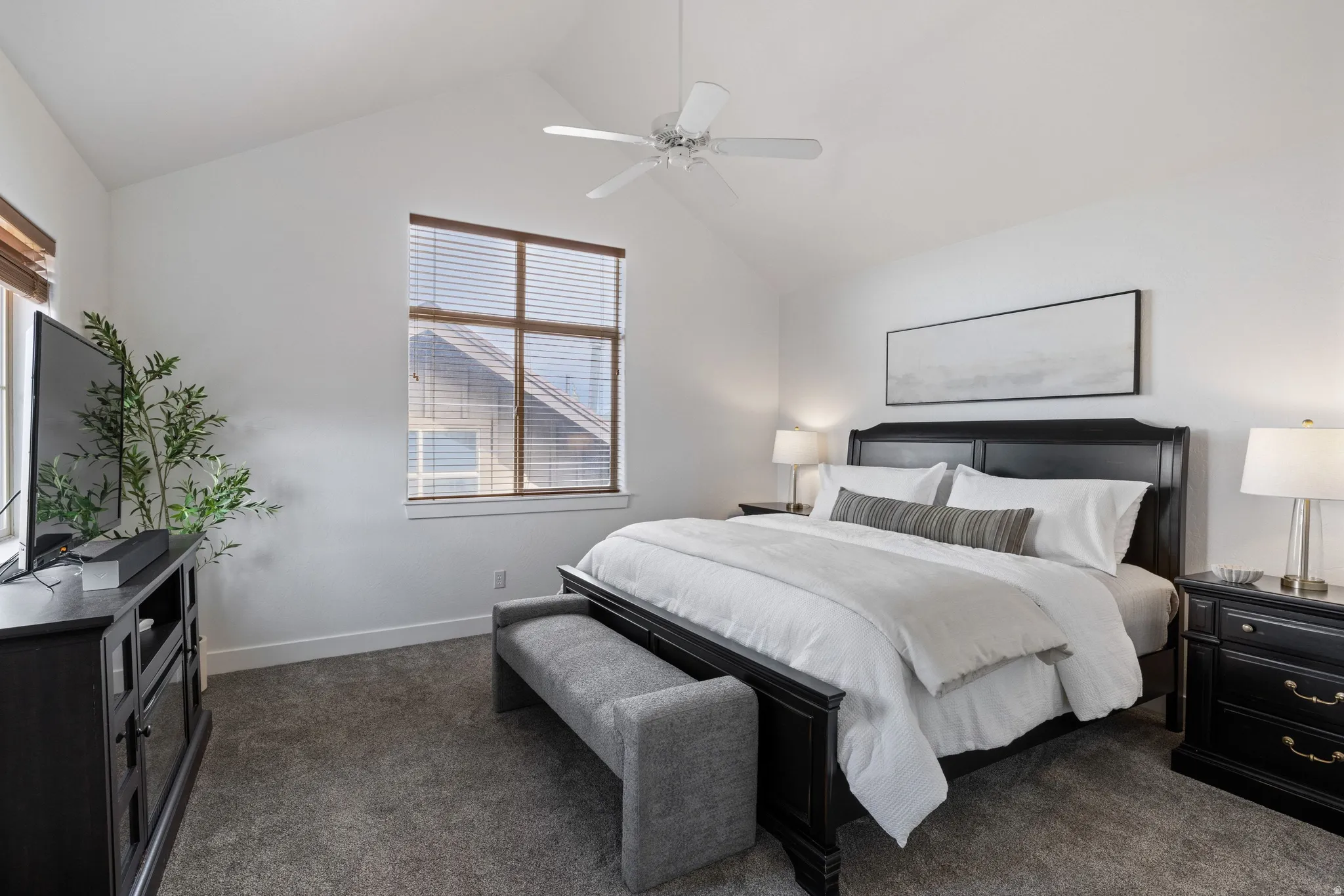 Vaulted ceiling room featuring a large window with wood-finish blinds, light grey carpeting, and a ceiling fan