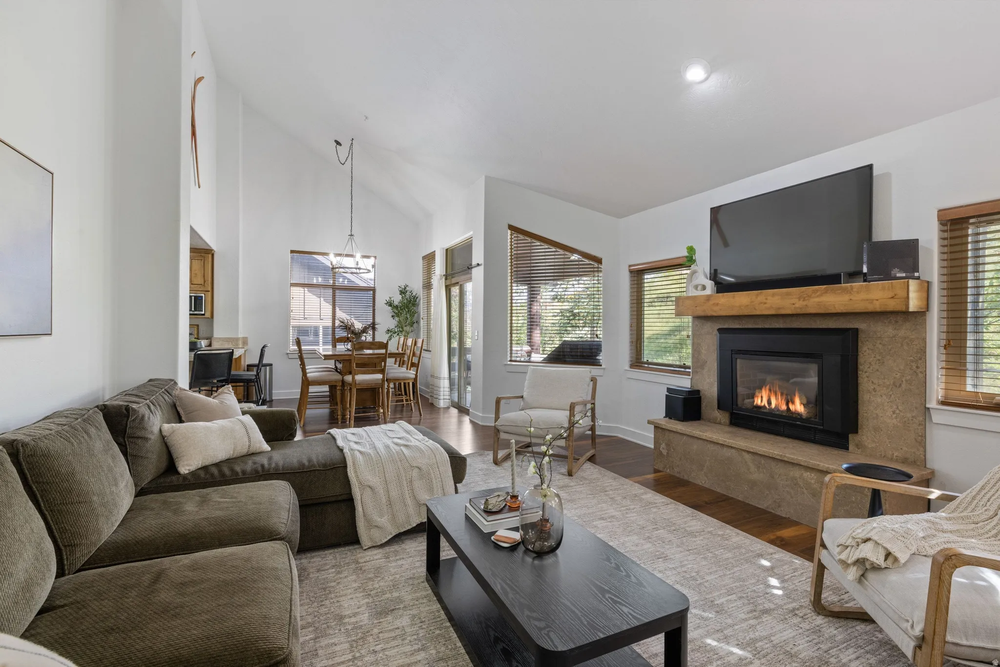 Living area featuring a stone-clad fireplace with wood mantle, vaulted ceilings, and wood-finish flooring