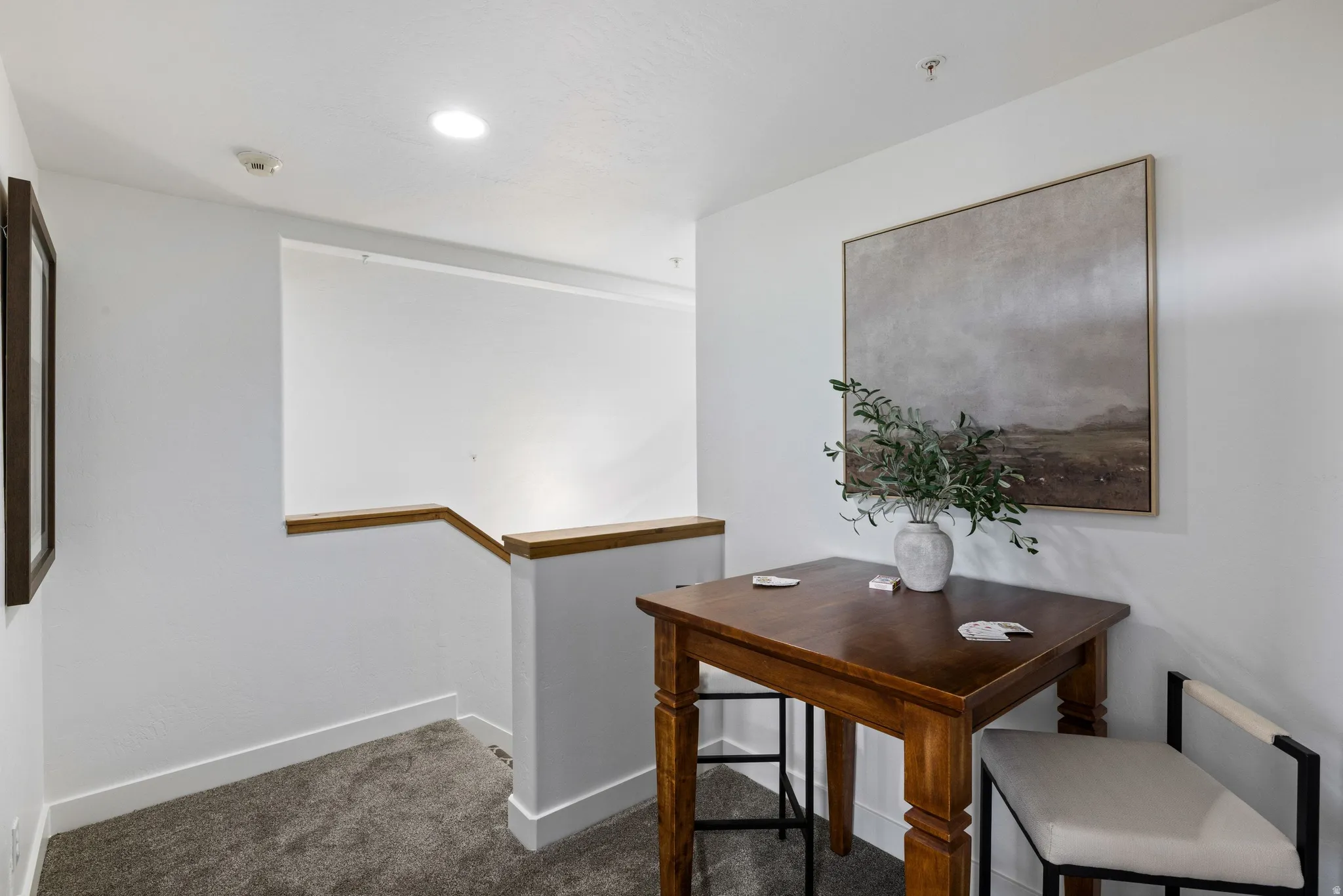 Carpeted hallway with white walls, wood handrail, and recessed ceiling lighting