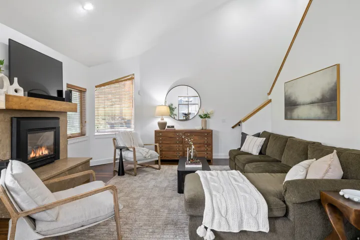 Living area featuring a stone-clad fireplace with a wood mantel, vaulted ceilings, and wood-finish flooring
