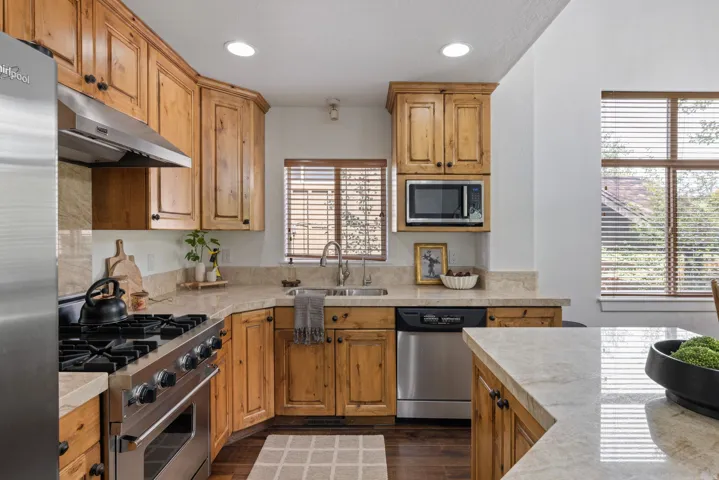 Kitchen featuring natural wood cabinetry, light-toned countertops, stainless steel appliances, and wood-finish flooring