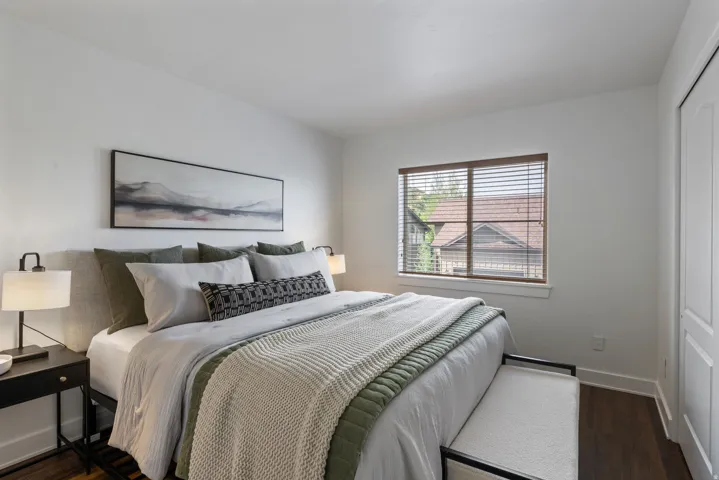 Bedroom featuring wood-finish flooring, white walls, and a window with wood blinds